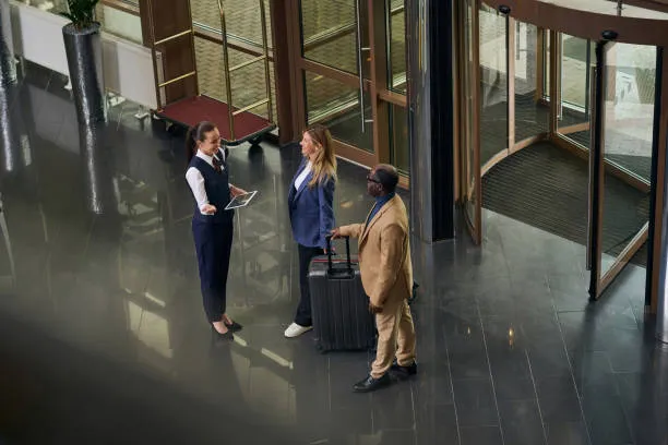 Mujer recibiendo a dos huéspedes con una tableta en la mano, demostrando cómo el software para hoteles mejora la gestión de reservas y servicios.