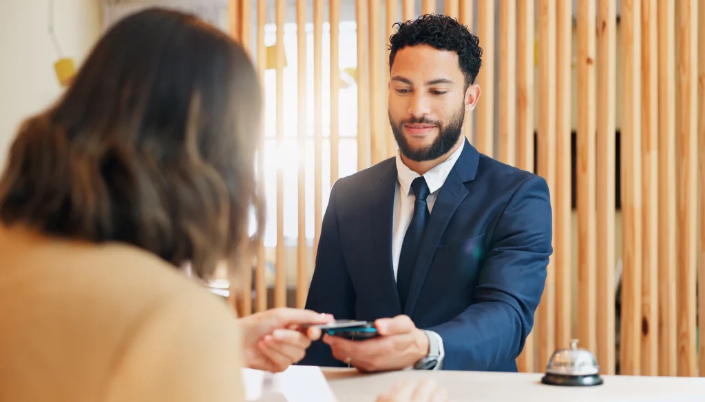 Recepcionista realizando el cobro a una huésped, con el apoyo de un software de administración hotelera que integra sistemas POS.