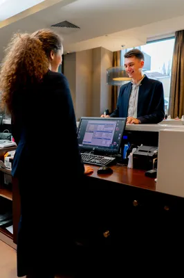 Punto de venta sobre el mostrador como elemento principal mientras una recepcionista atiende de espaldas a un huésped en hotel que usa software hotelero