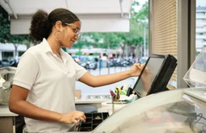 Mujer de perfil interactuando con la pantalla del punto de venta dentro de un hotel que utiliza software hotelero