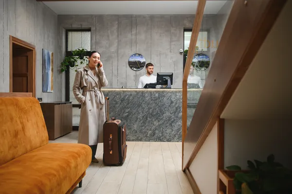 Recepción de hotel boutique con recepcionista y huésped hablando por teléfono mientras se gestiona reservación desde el motor de reservas