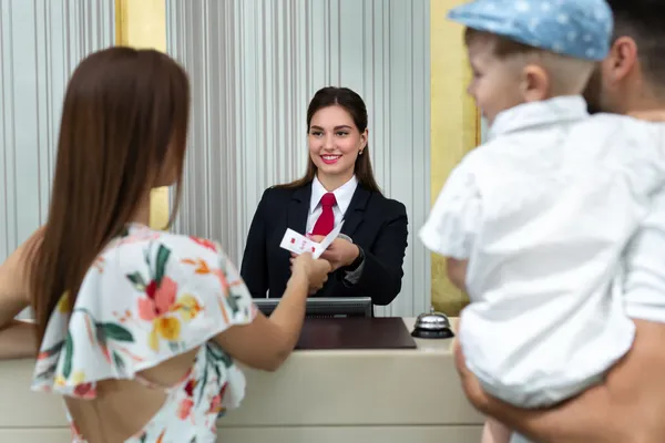 Recepcionista entregando tarjeta llave a familia con niño pequeño después de usar el motor de reservas para planear sus vacaciones