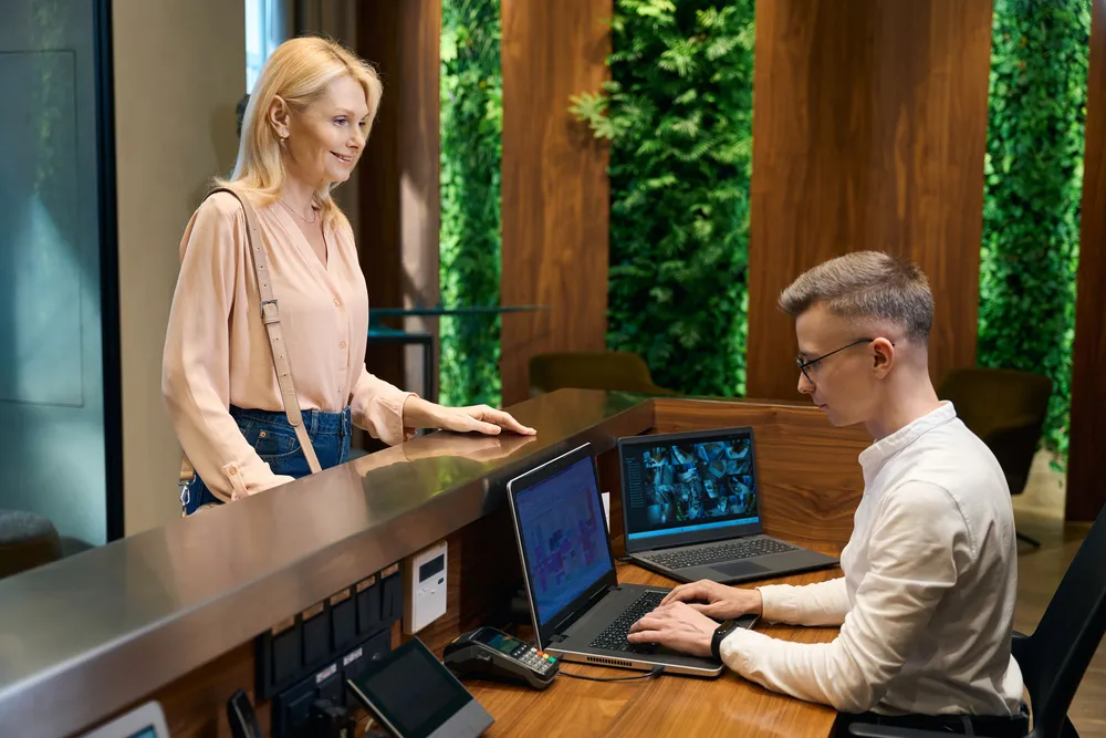 Fotografía de una mujer y un recepcionista de hotel trabajando con ciberseguridad en sistemas hoteleros