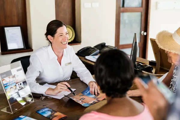 Foto de una recepcionista que utiliza un motor de reservas para el hotel atendiendo a dos huéspedes